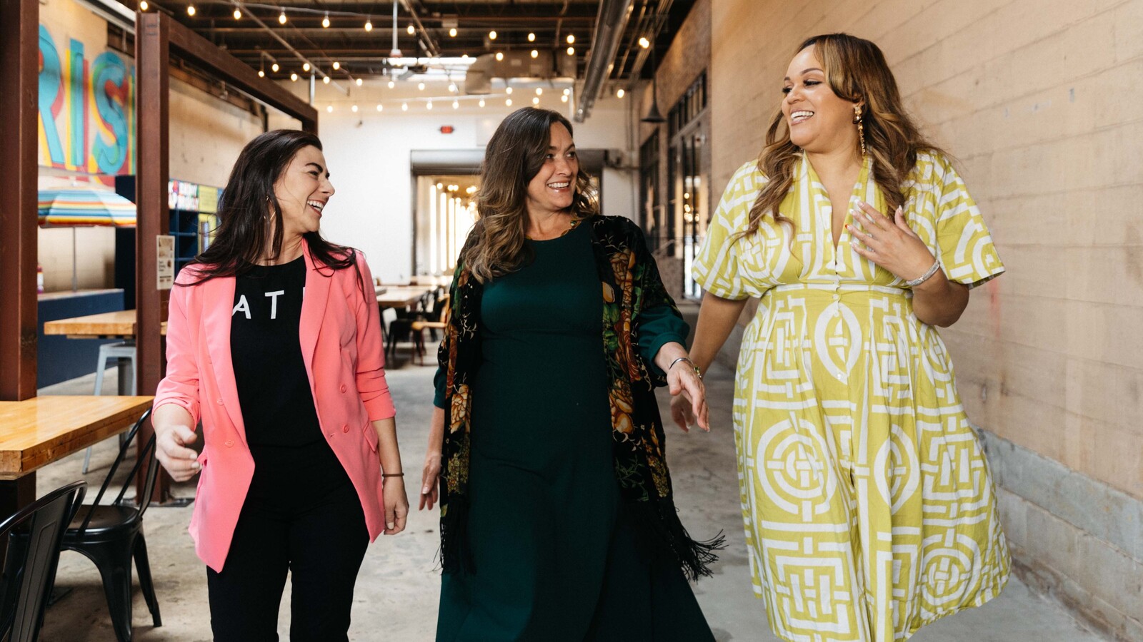 Three women walking and laughing together in a bright industrial venue space